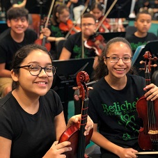 Two female students smiling while sitting with orchestra